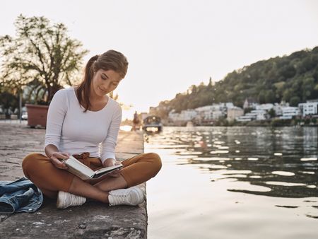 Frau sitzt mit Buch am Neckar