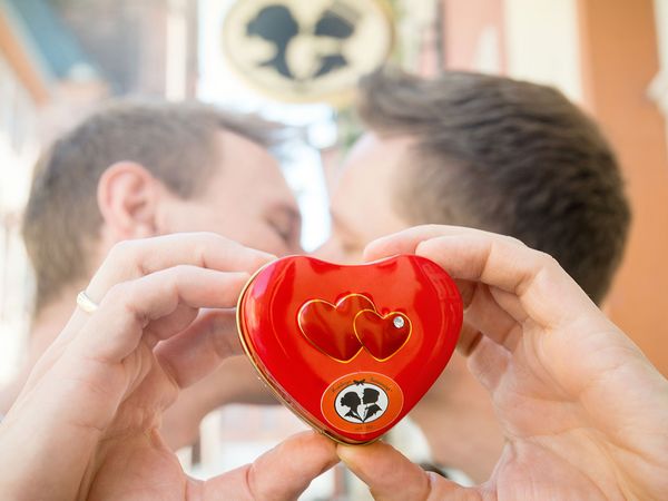 2 men kissing behind a metal box filled with reginal candy.